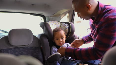 Tired-boy-sitting-in-baby-seat,-father-fastening-seat-belts